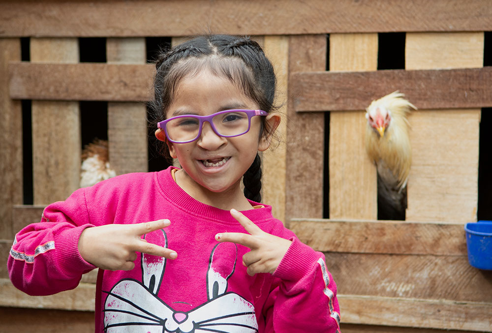 Kristhell flashing two peace signs in front of a chicken coop